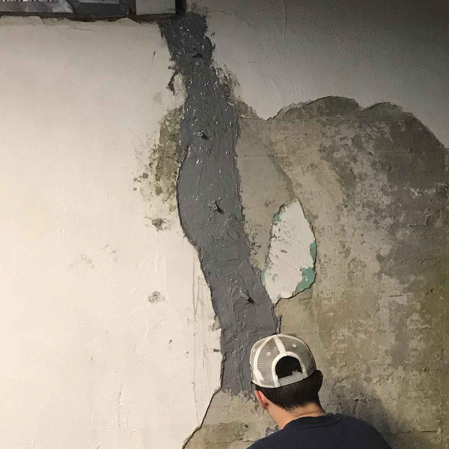 Person patching a cracked concrete wall with gray sealant.