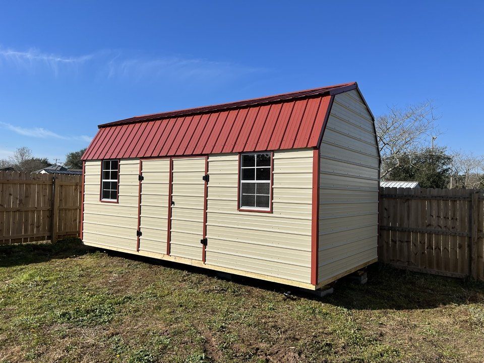 A white barn with a red roof is sitting in the grass next to a wooden fence.