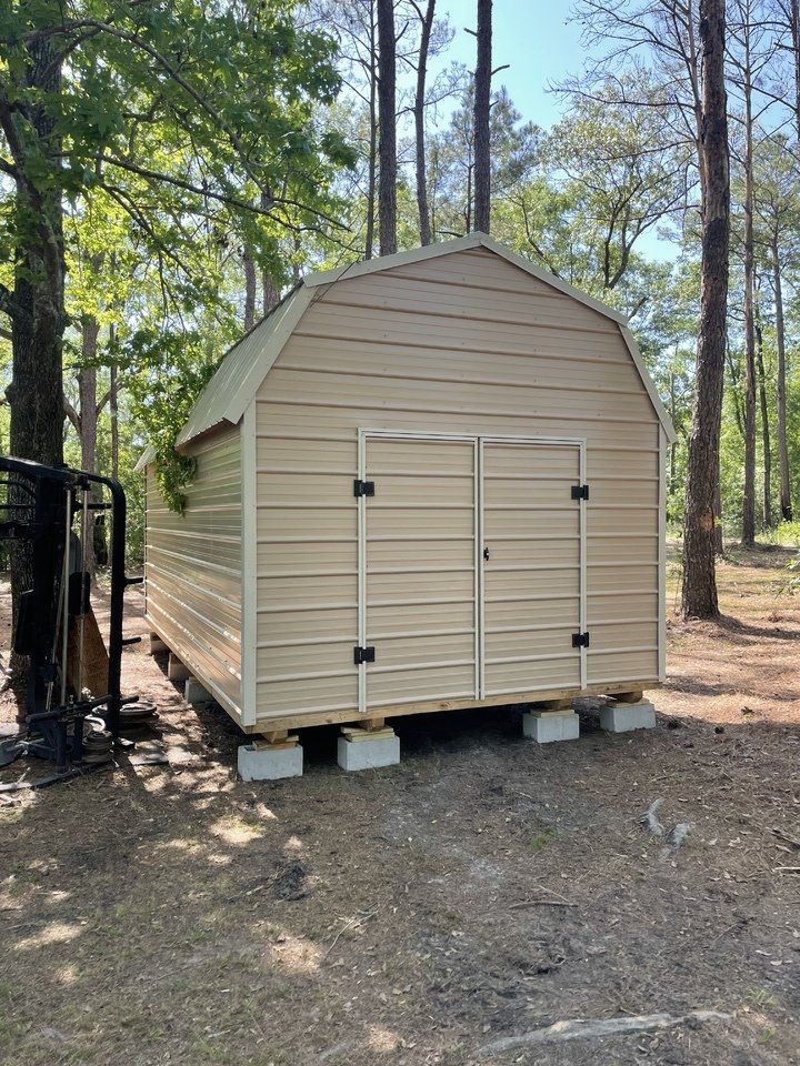 A barn is sitting on concrete blocks in the middle of a forest.