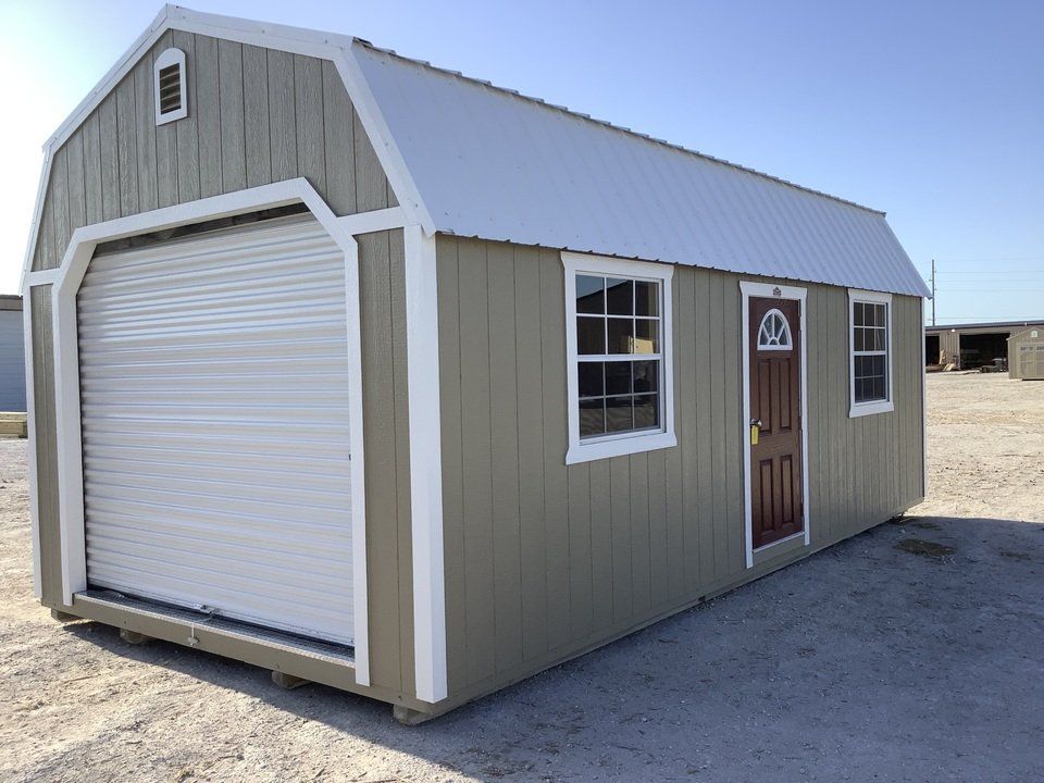A red barn with a white garage door is sitting in the middle of a grassy field.