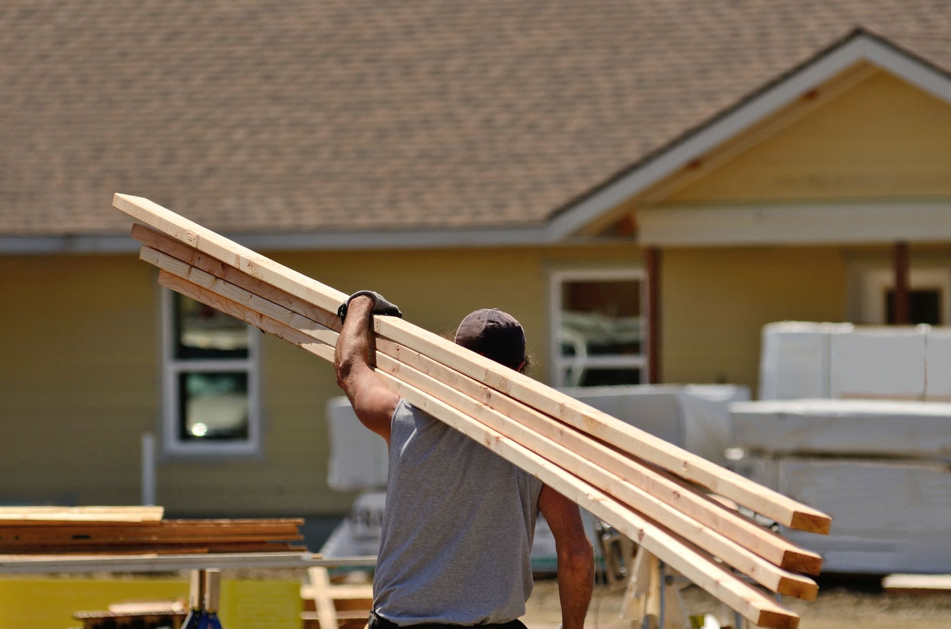 A man is carrying a stack of wood in front of a house under construction