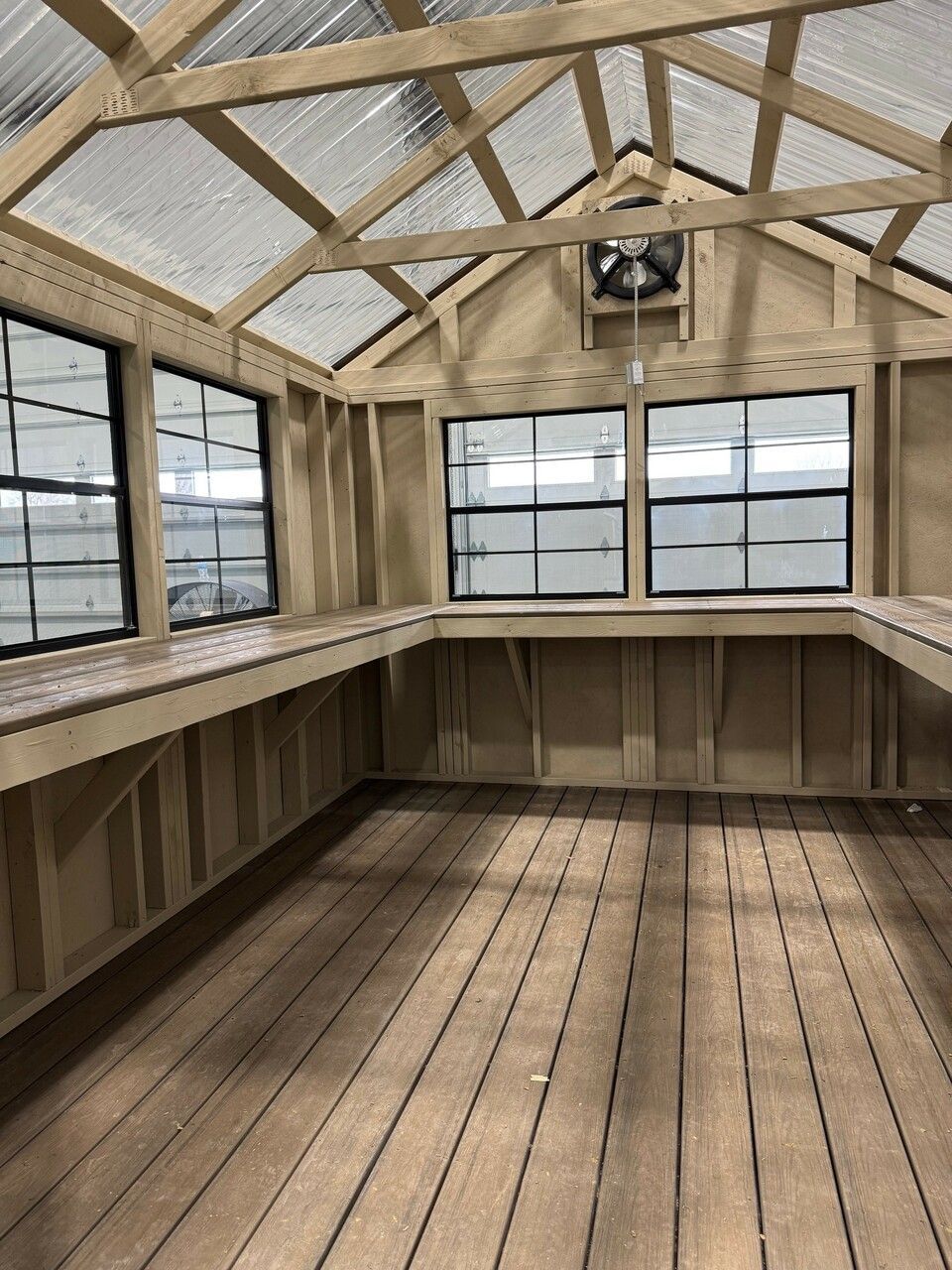 A greenhouse with wooden floors and a fan on the ceiling.
