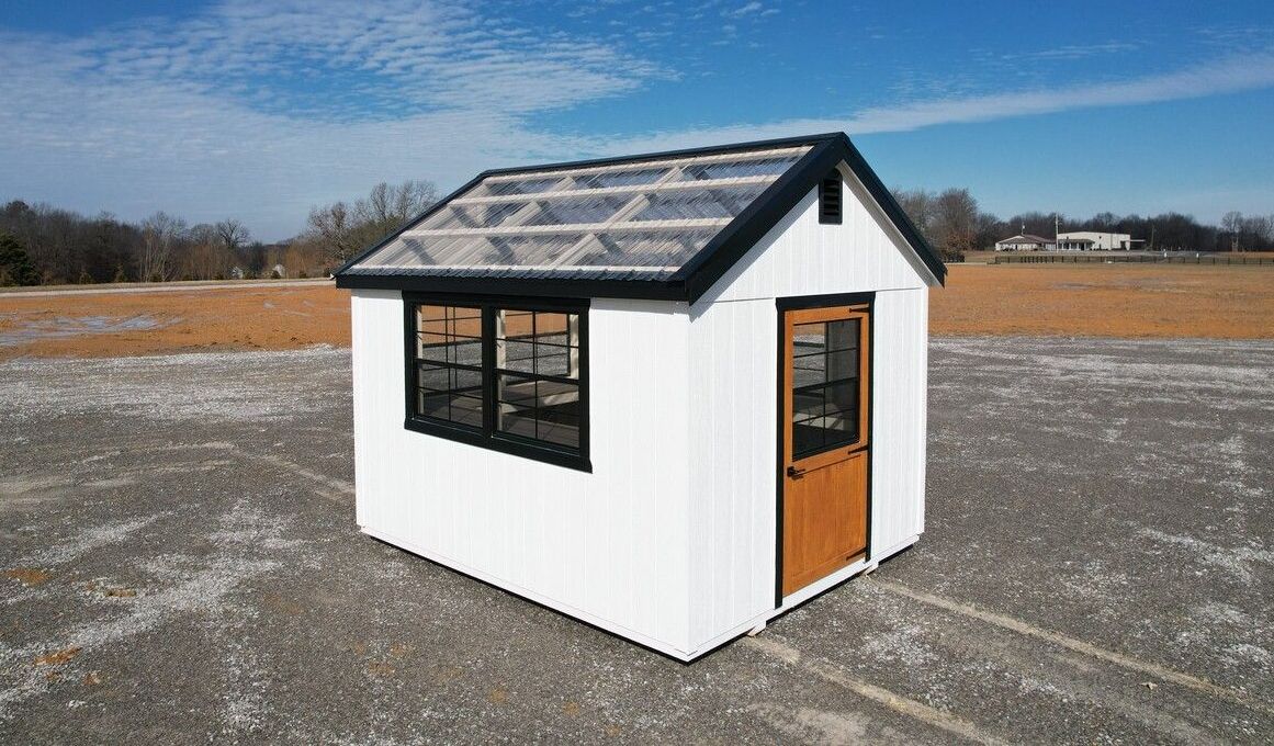 A small white shed with a black roof is sitting on top of a dirt field.