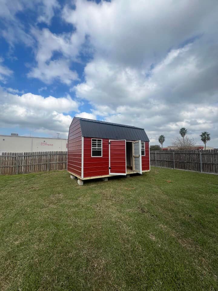 A red shed with a white roof and windows is sitting in the grass.