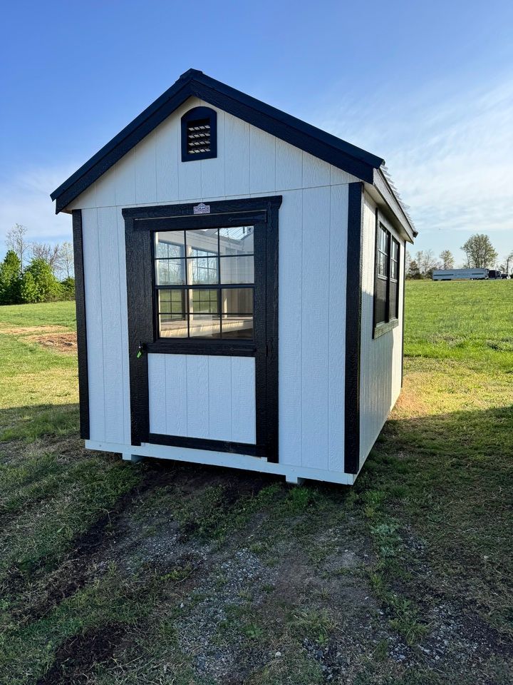 A white greenhouse with black trim is sitting in the middle of a grassy field.