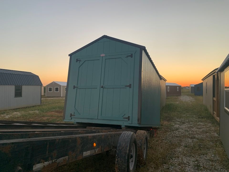 A teal shed on a trailer, ready for transport, in a field at dusk.