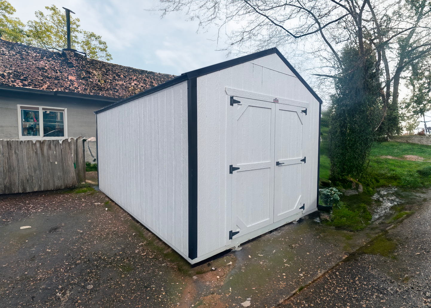 A small white shed is sitting in the middle of a dirt field.