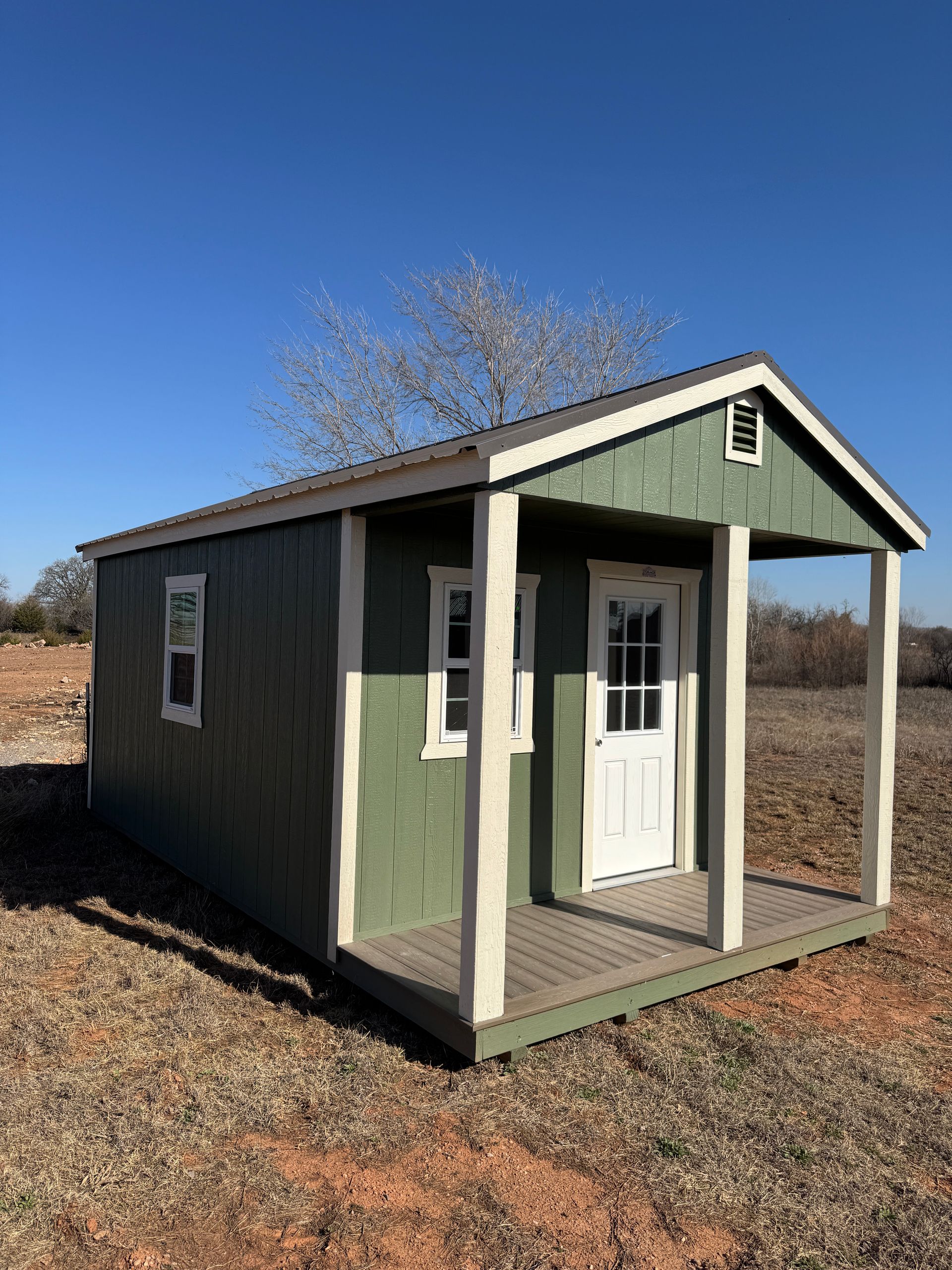 A green shed with a porch in the middle of a field.