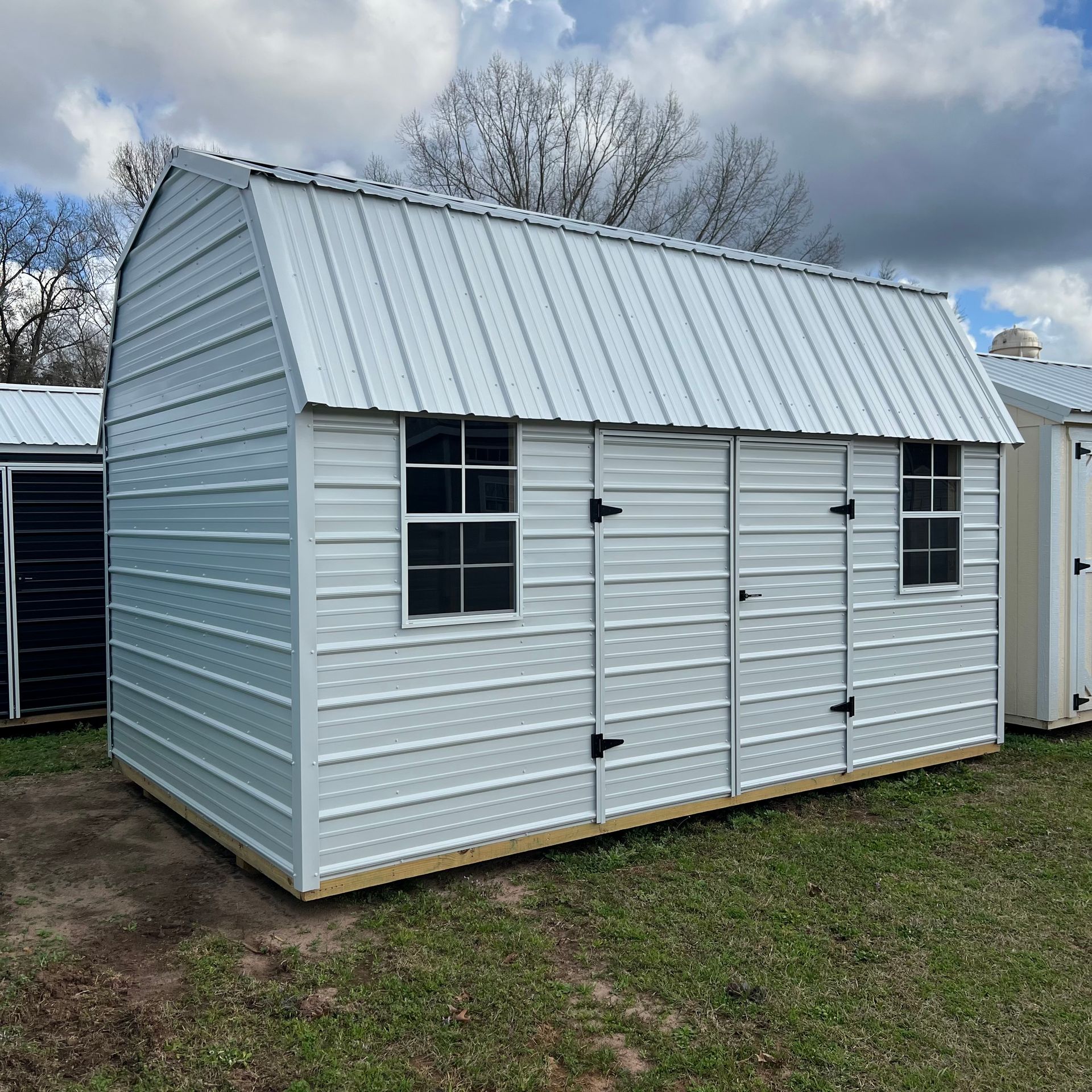 A white shed with a metal roof is sitting in the middle of a grassy field.