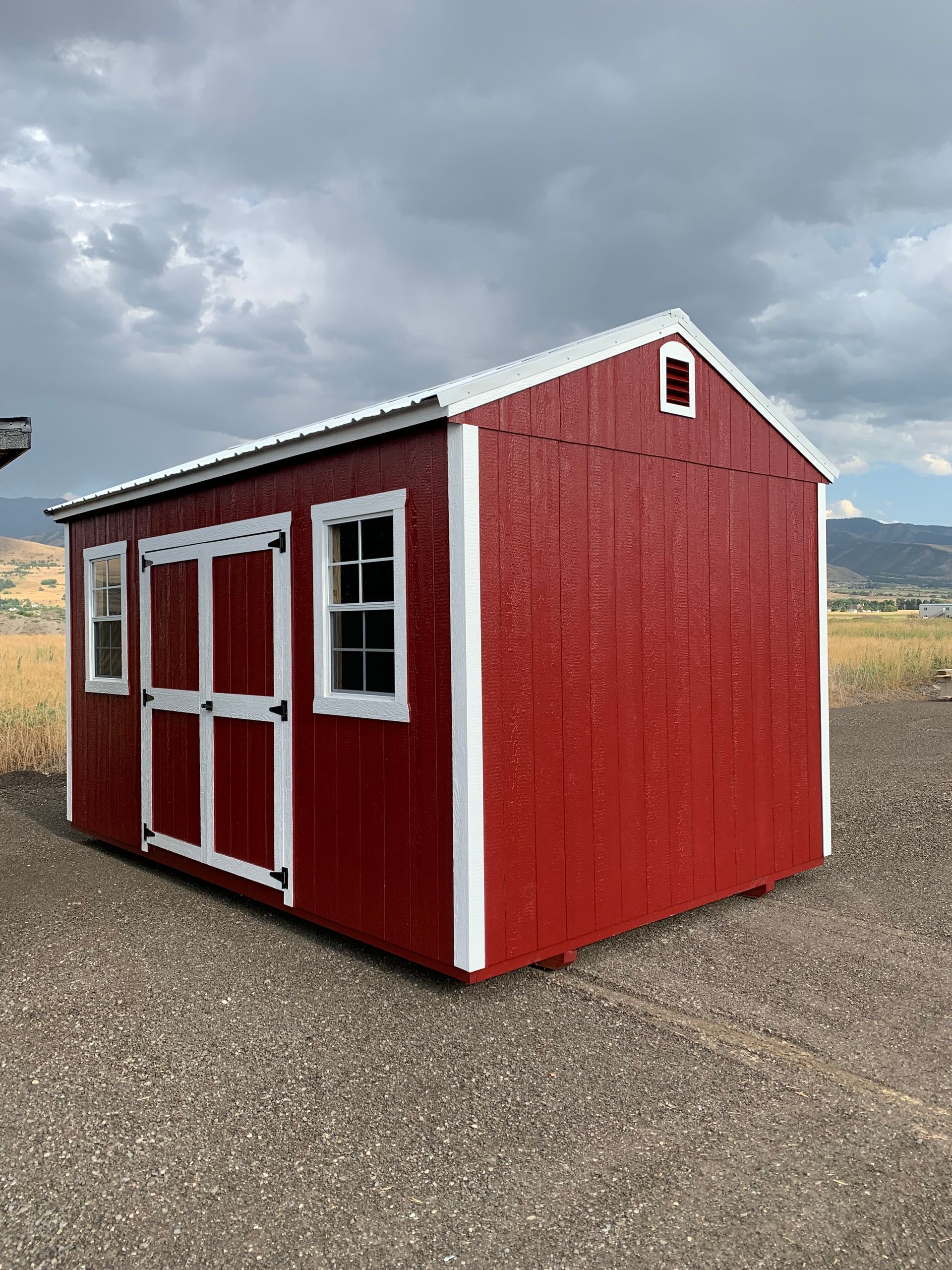 A green shed with white windows is sitting in the middle of a grassy field.