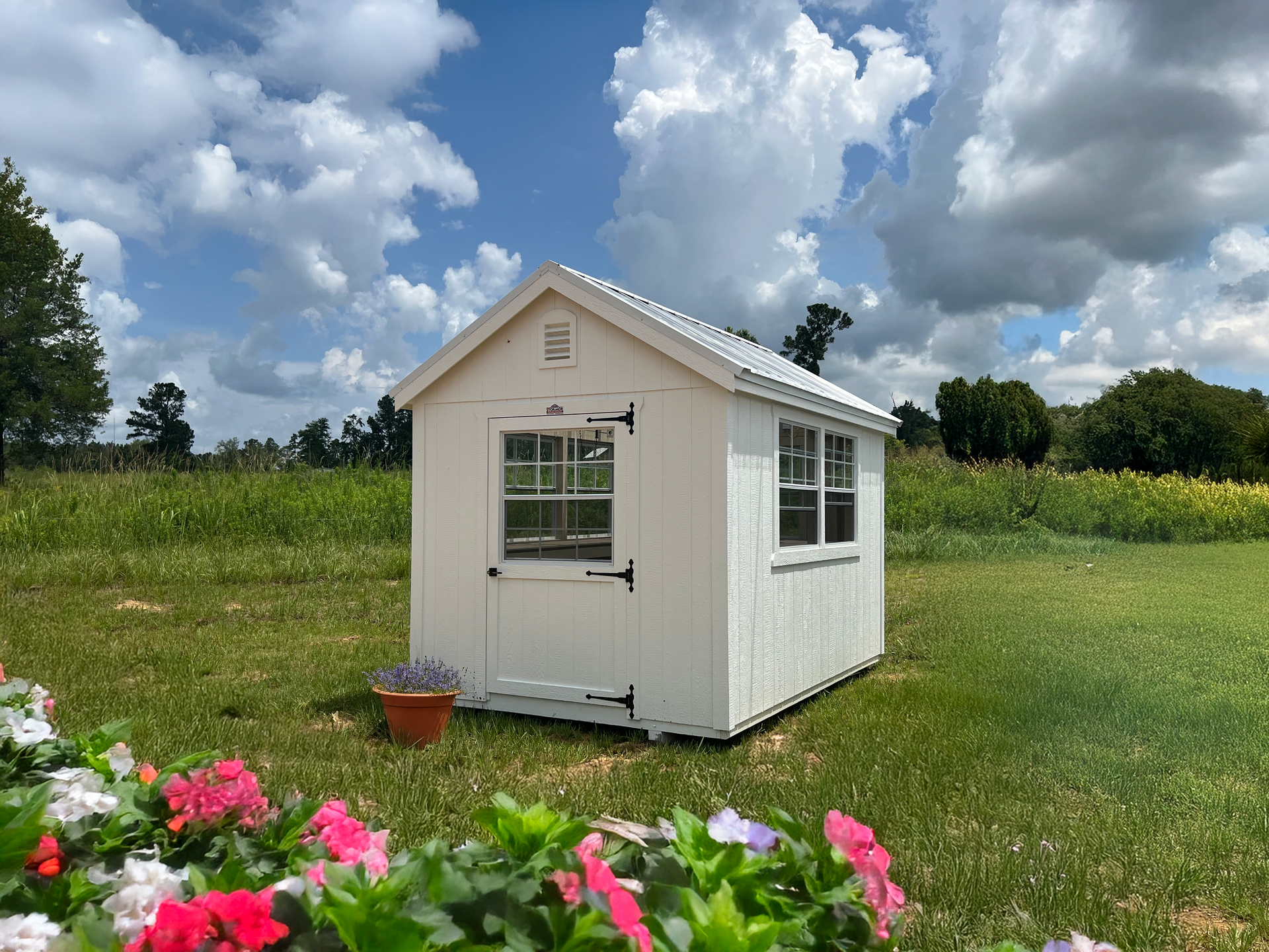 A white greenhouse shed is sitting in the middle of a grassy field.