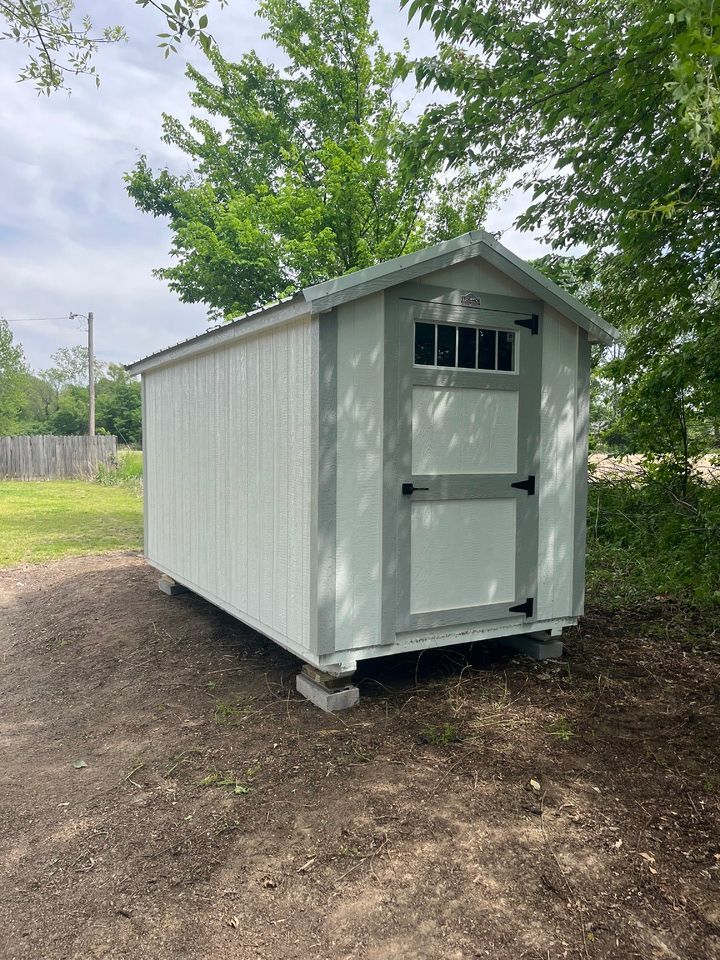 A small white shed is sitting in the middle of a dirt field.