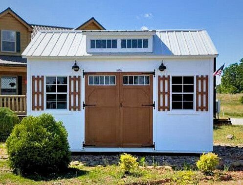 A white shed with brown doors and windows is sitting in front of a house.