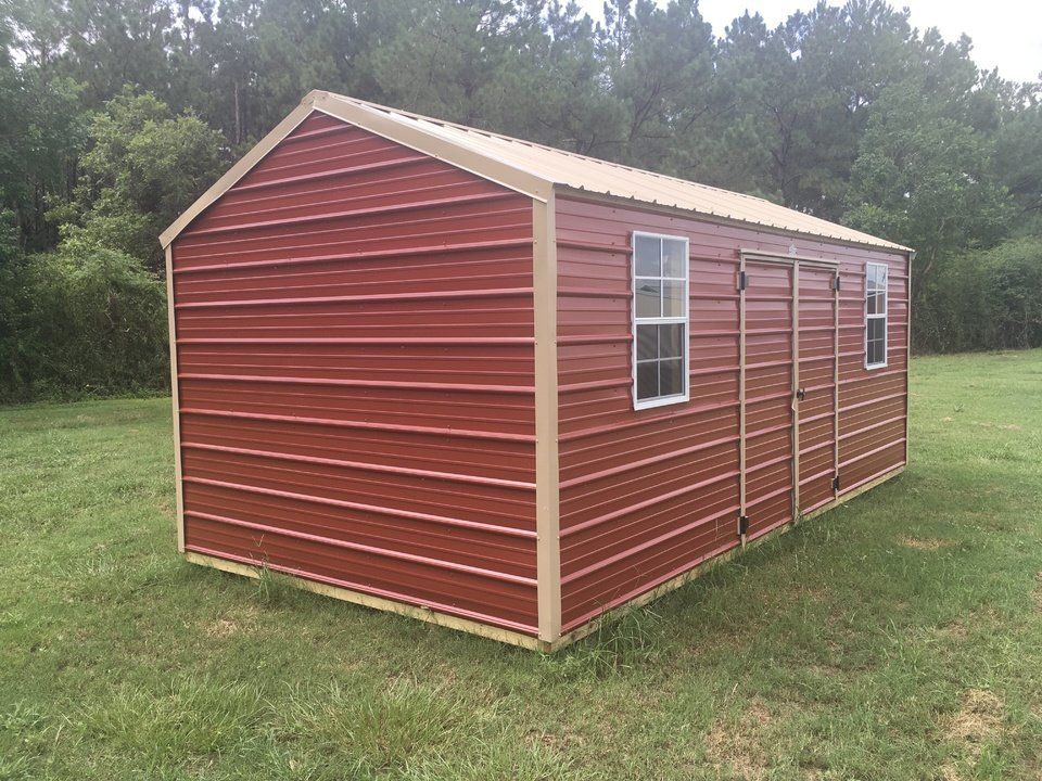 A red metal shed is sitting in the middle of a grassy field.