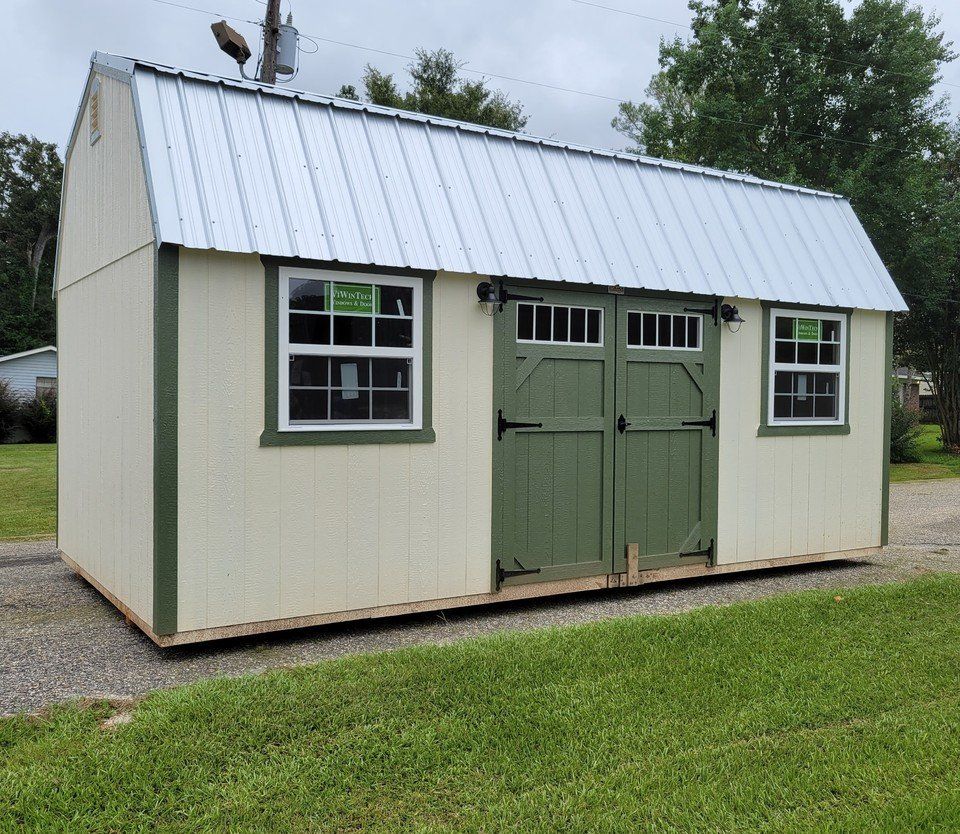 A white barn with green doors and windows is sitting on top of a lush green field.
