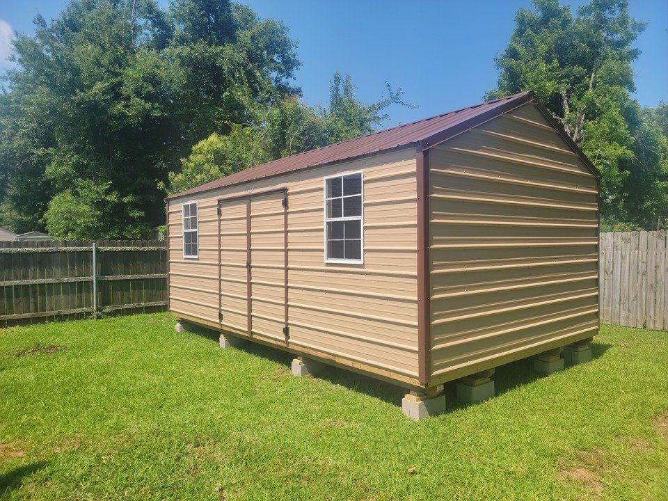 A metal shed with two windows is sitting in the middle of a grassy field.