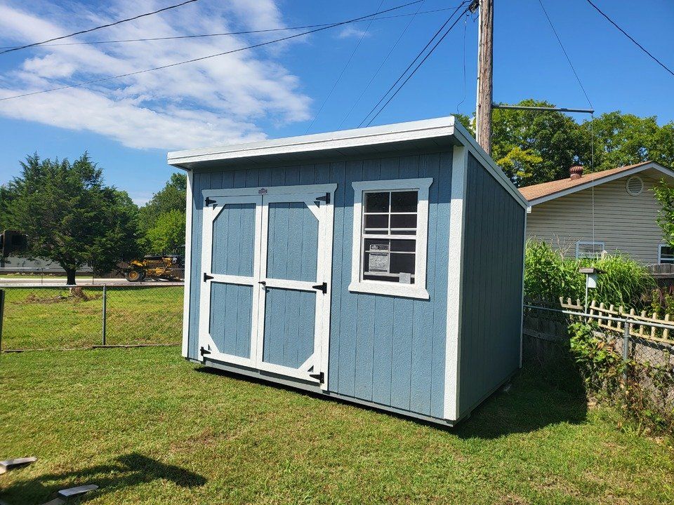 A blue and white shed is sitting in the grass in front of a house.
