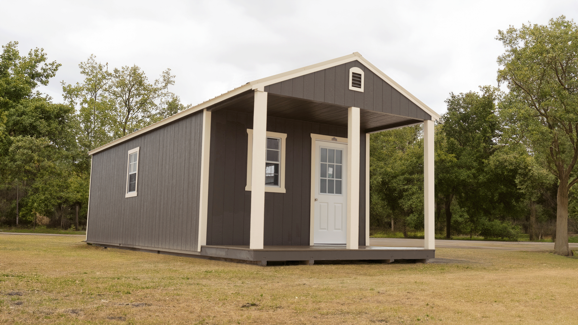 A cabin with a porch is sitting in the middle of a field.