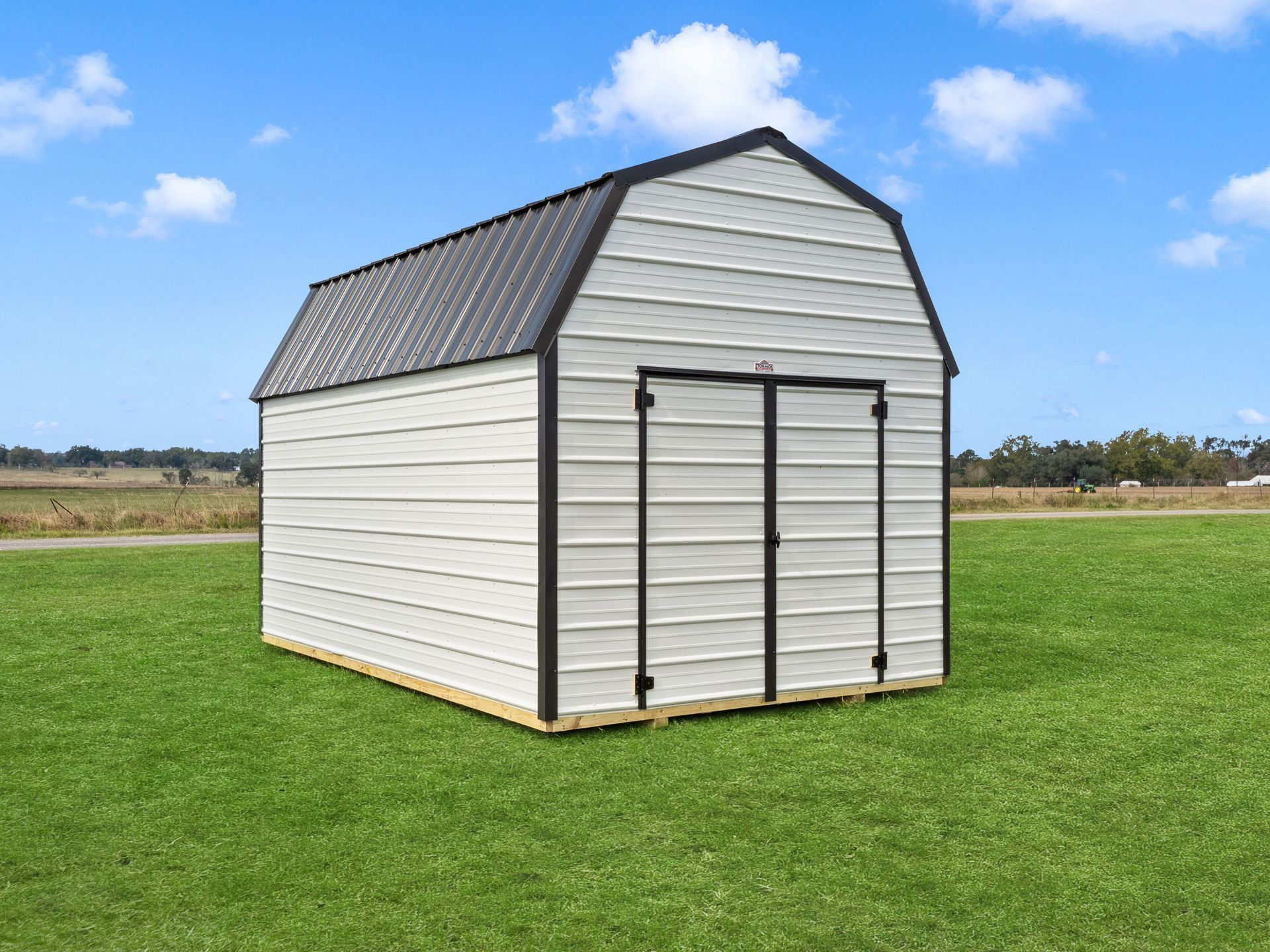A white barn with a black roof is sitting on top of a lush green field.