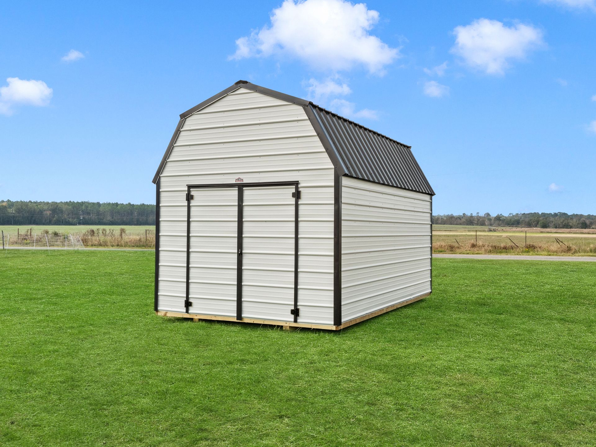 A white barn shed is sitting in the middle of a grassy field.