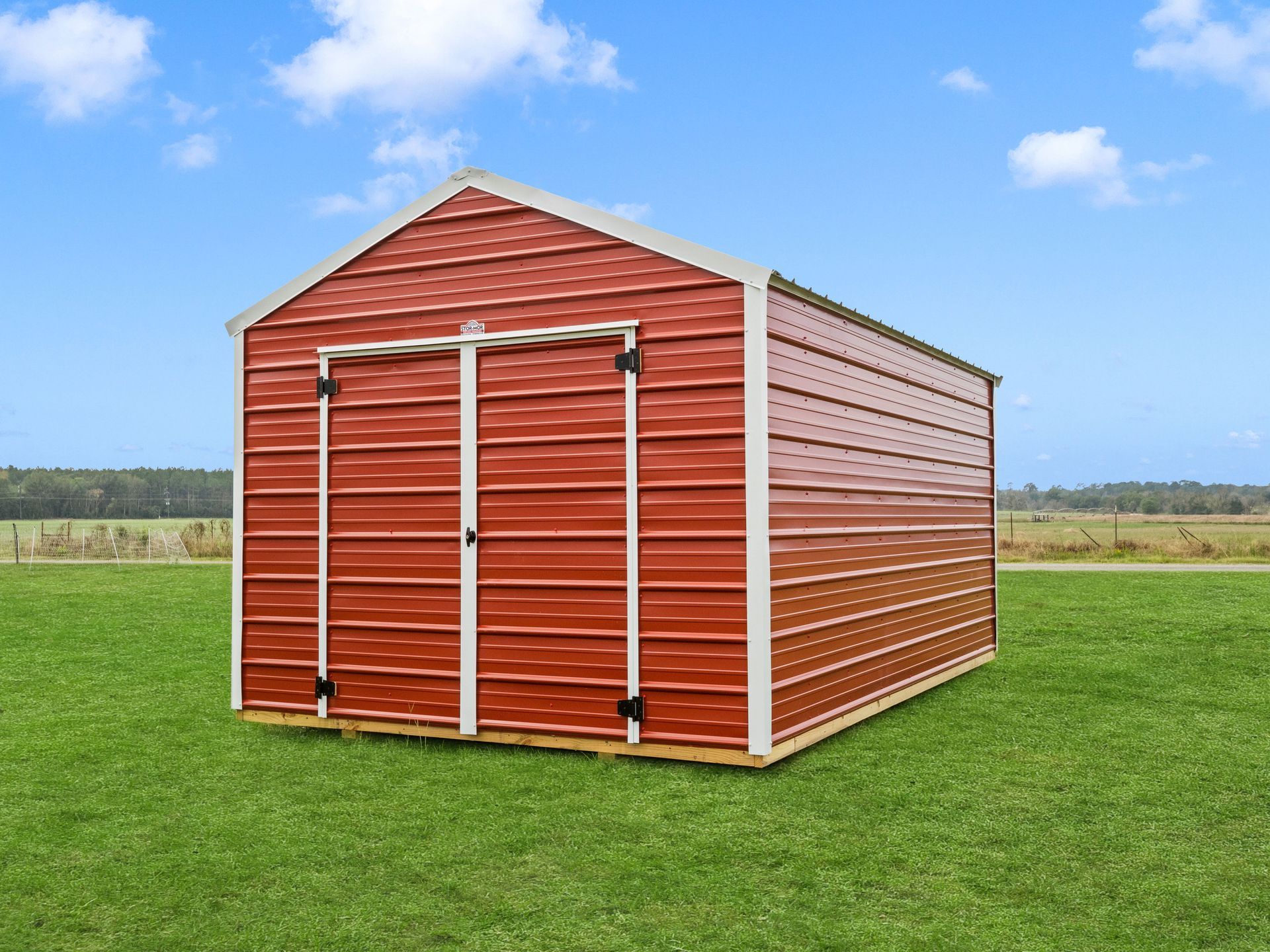 A green metal shed with white trim is sitting on top of a dirt field.