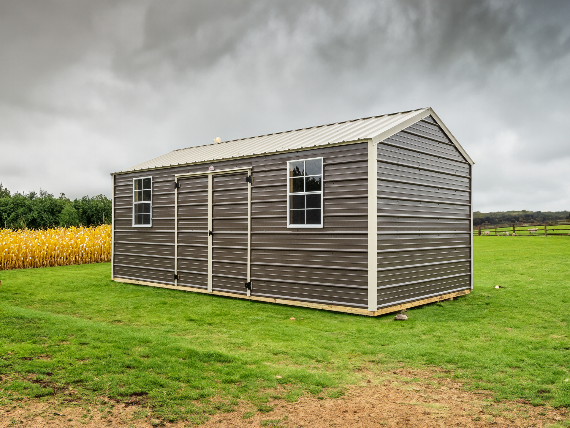A metal shed with two windows is sitting in the middle of a grassy field.