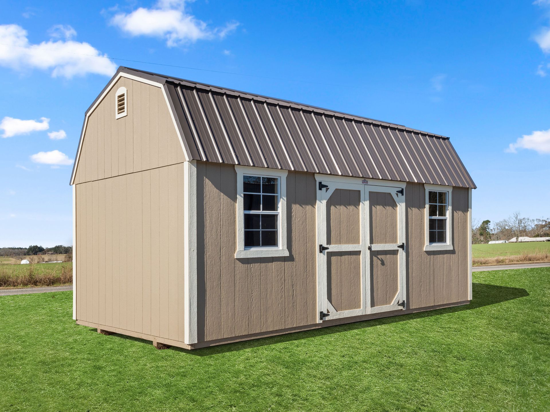 A small barn with a metal roof is sitting on top of a lush green field.