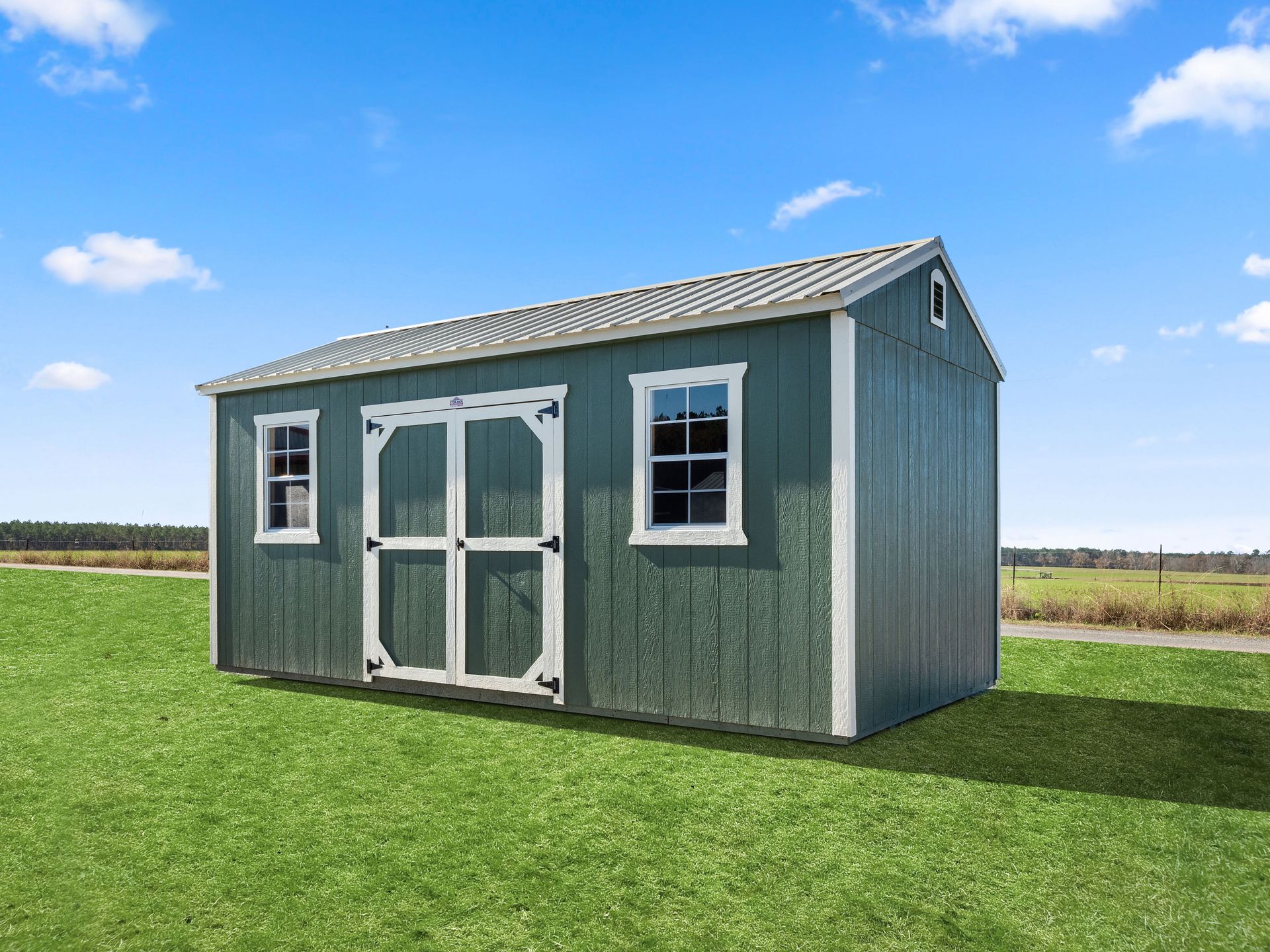 A green shed with white trim and windows is sitting on top of a lush green field.