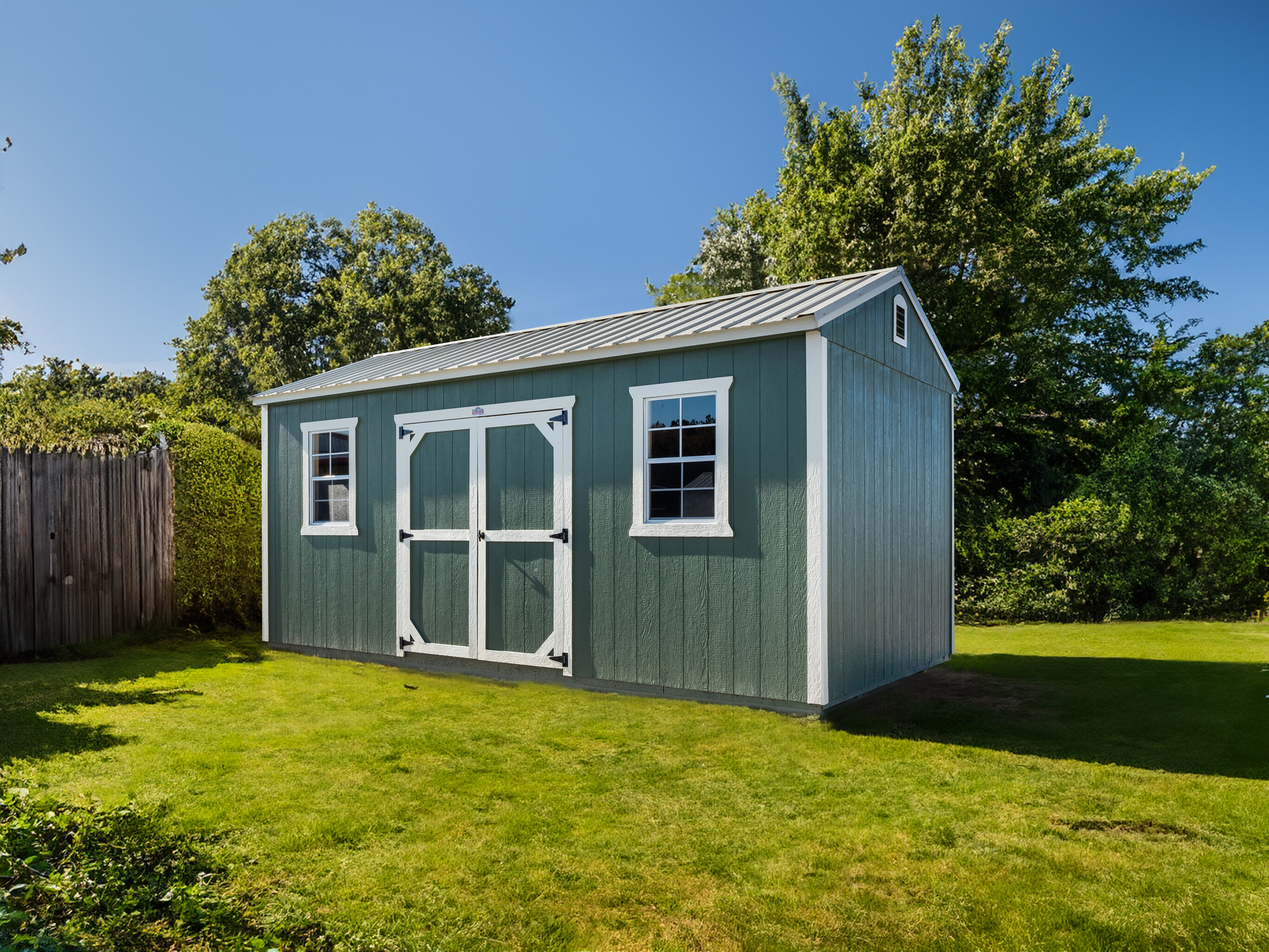 A green shed with white trim is sitting in the middle of a lush green yard.