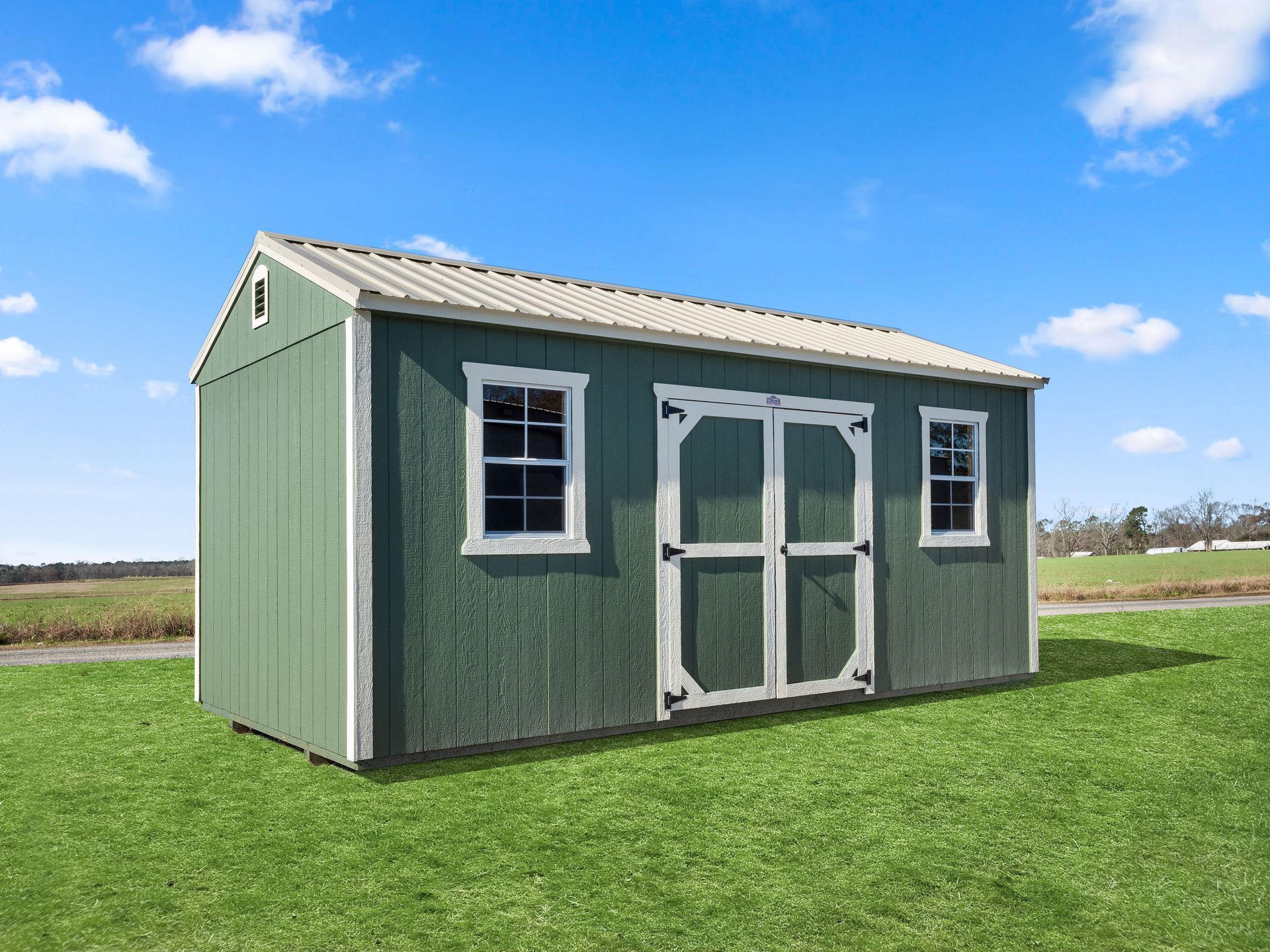 A green shed with white trim and windows is sitting on top of a lush green field.