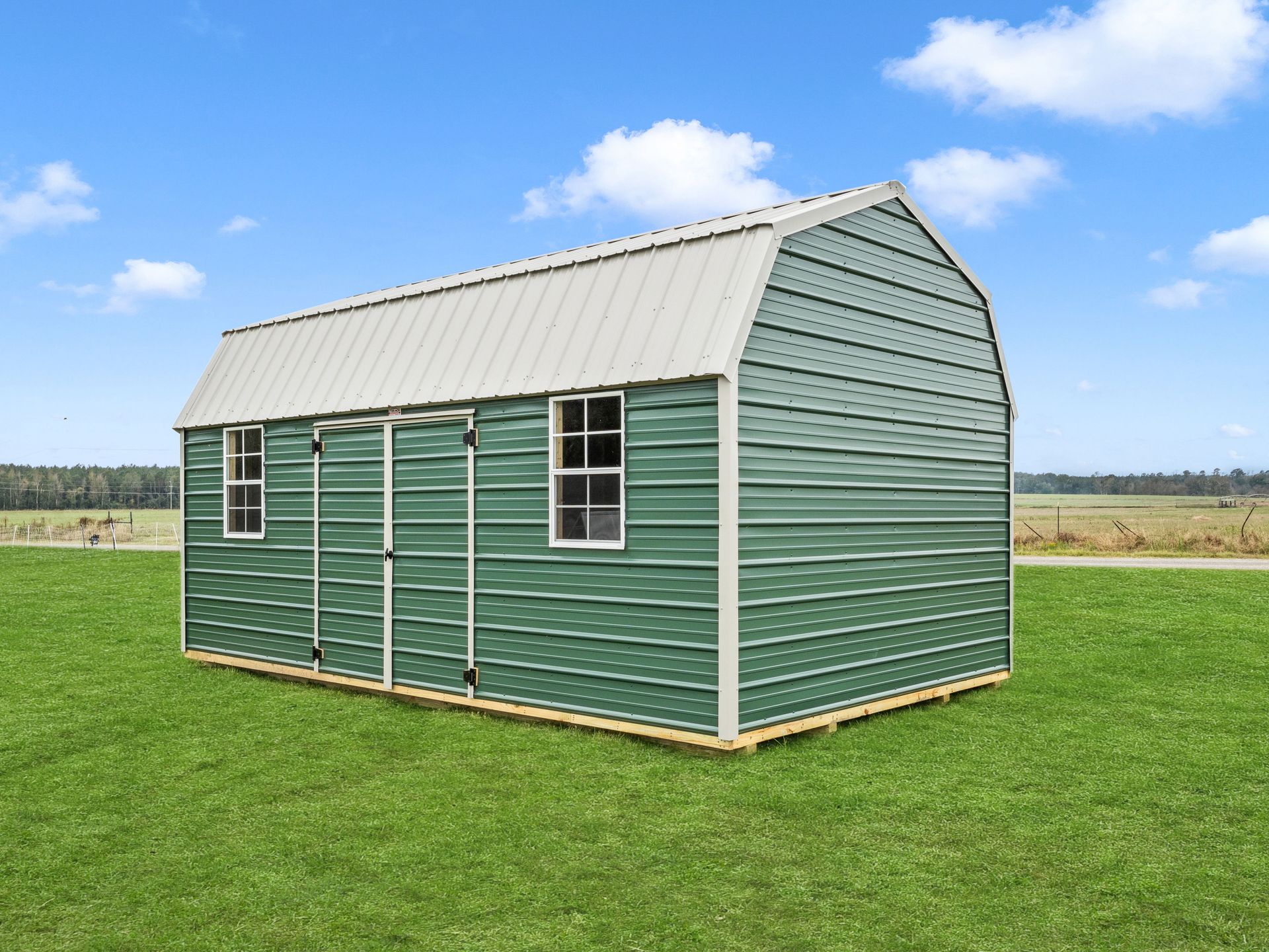 A green barn with a white roof is sitting on top of a lush green field.