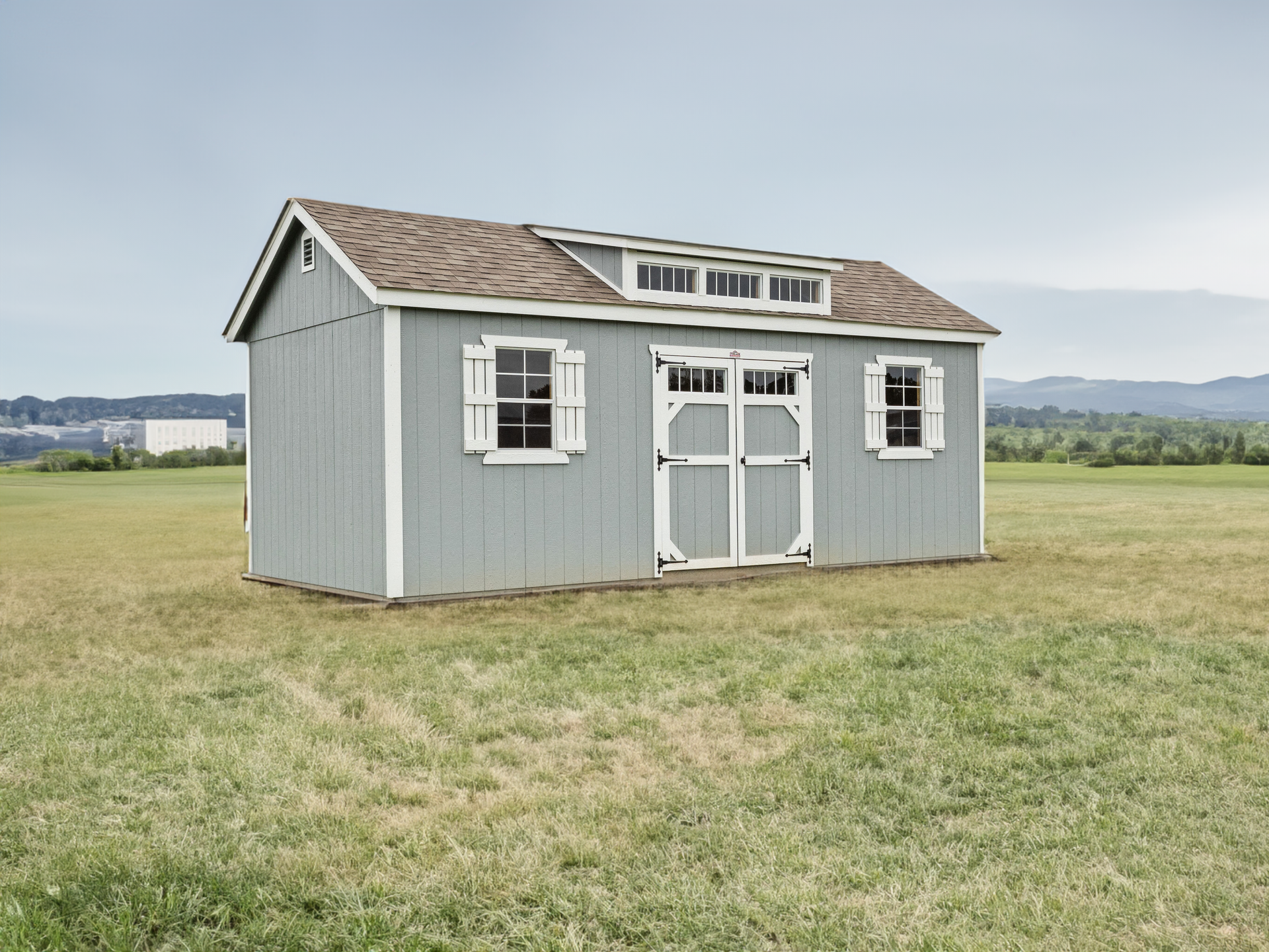 A gray shed with a brown roof is sitting in the middle of a grassy field.