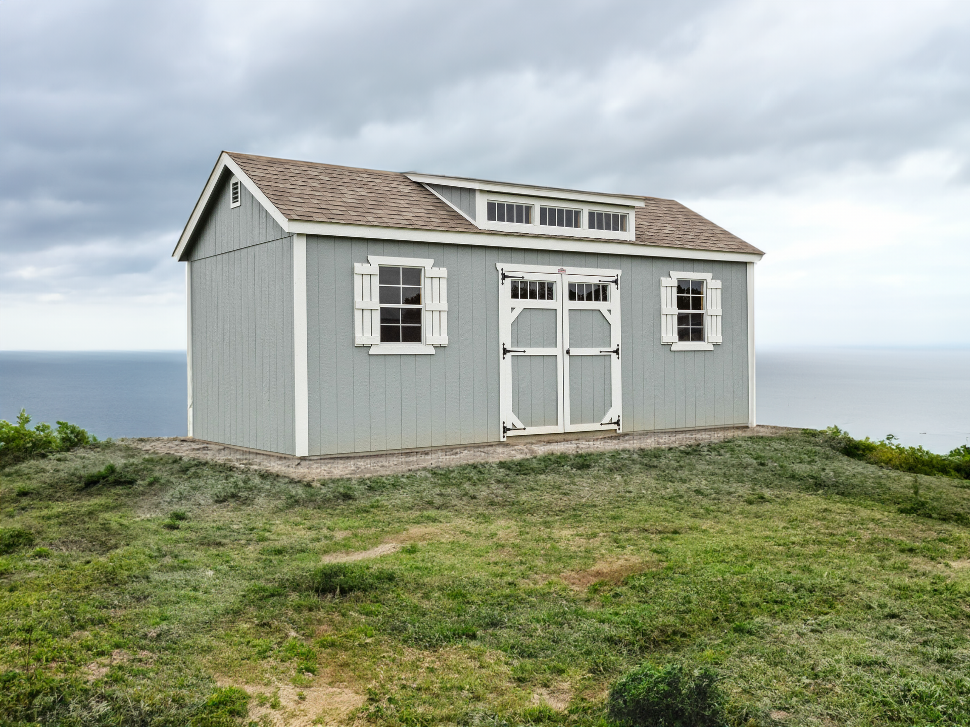 A small shed is sitting on top of a grassy hill overlooking the ocean.