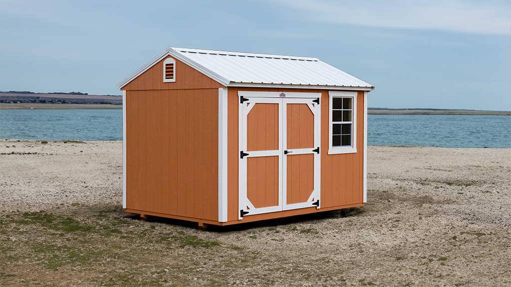 A small orange shed is sitting on a sandy beach near the water.