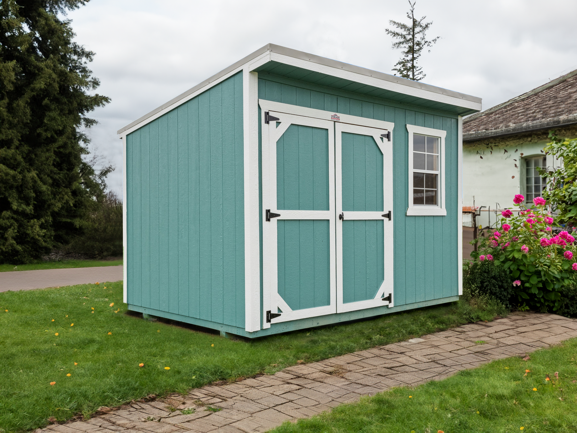A green and white shed is sitting on top of a lush green lawn next to a house.