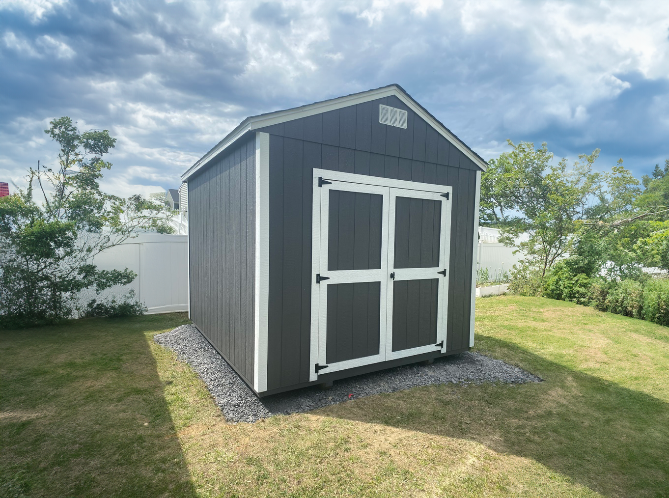 A black and white shed is sitting in the middle of a grassy yard.