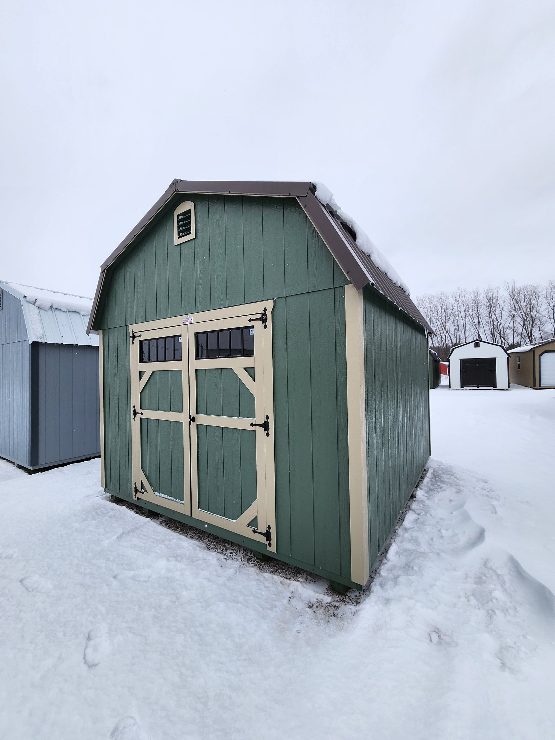 A green and white barn shed is sitting in the middle of a grassy field.