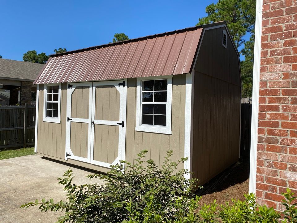 A barn shed with a brown roof is next to a brick building.