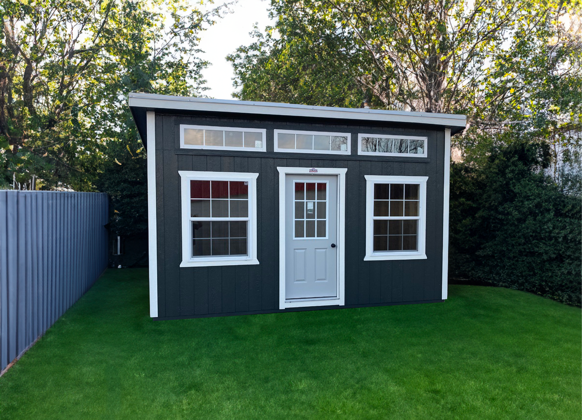 A small shed with a white door and windows in a backyard.