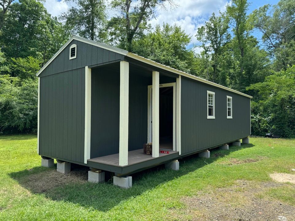 A small house with a porch is sitting in the middle of a grassy field.