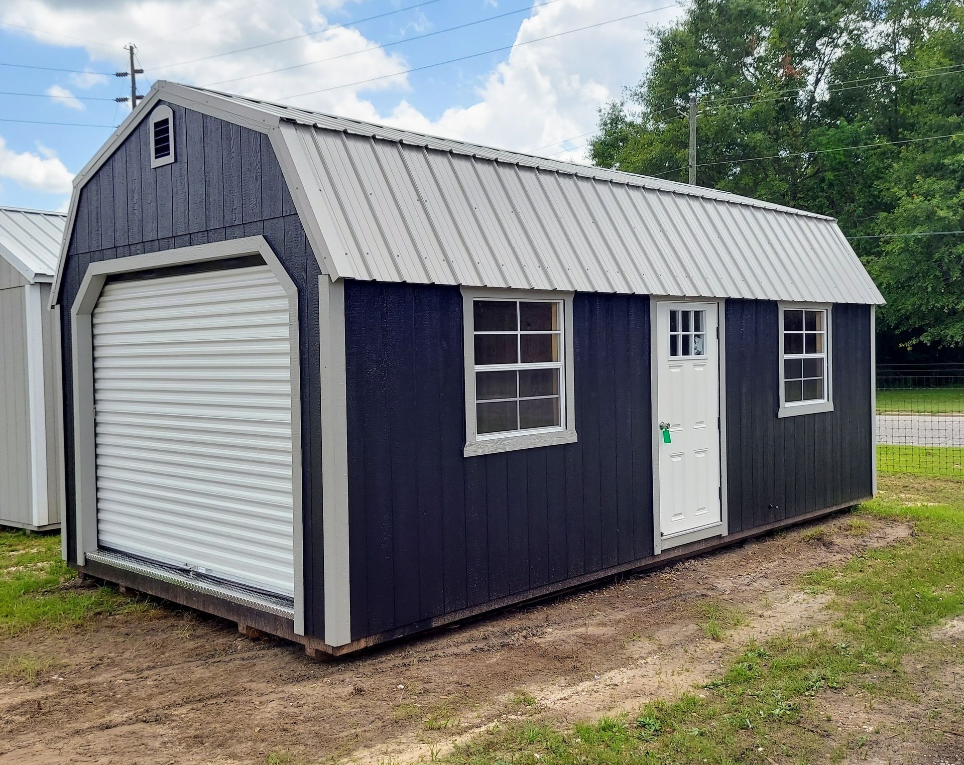 A black and white barn with a garage door is sitting in the middle of a grassy field.