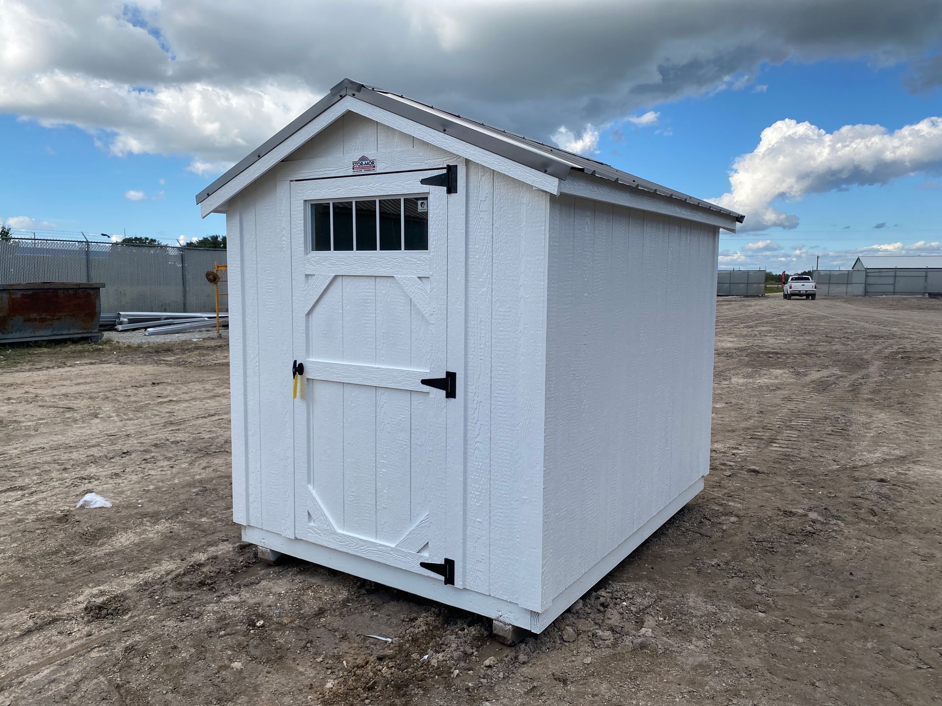 A small white shed is sitting in the middle of a dirt field.
