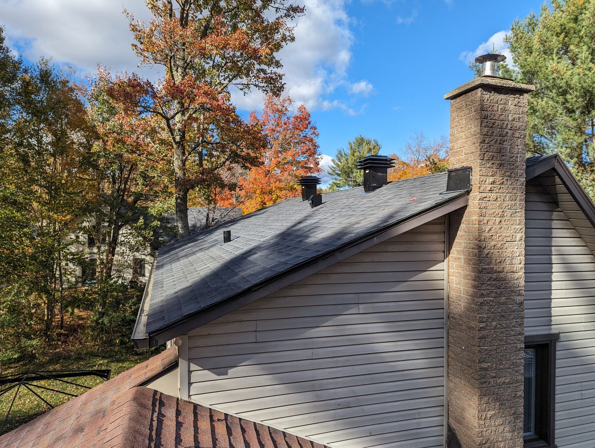Toit de maison avec deux cheminées à côté d'arbres aux couleurs automnales sous un ciel bleu