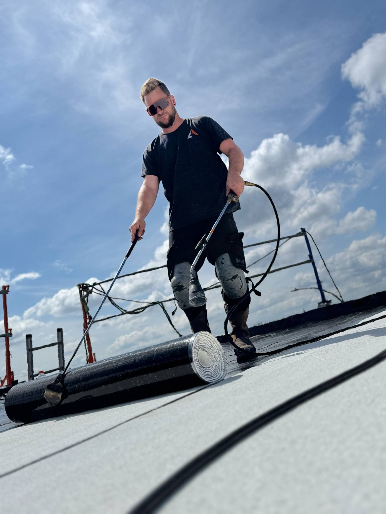 Une personne travaille sur un toit avec des outils sous un ciel bleu et des nuages.