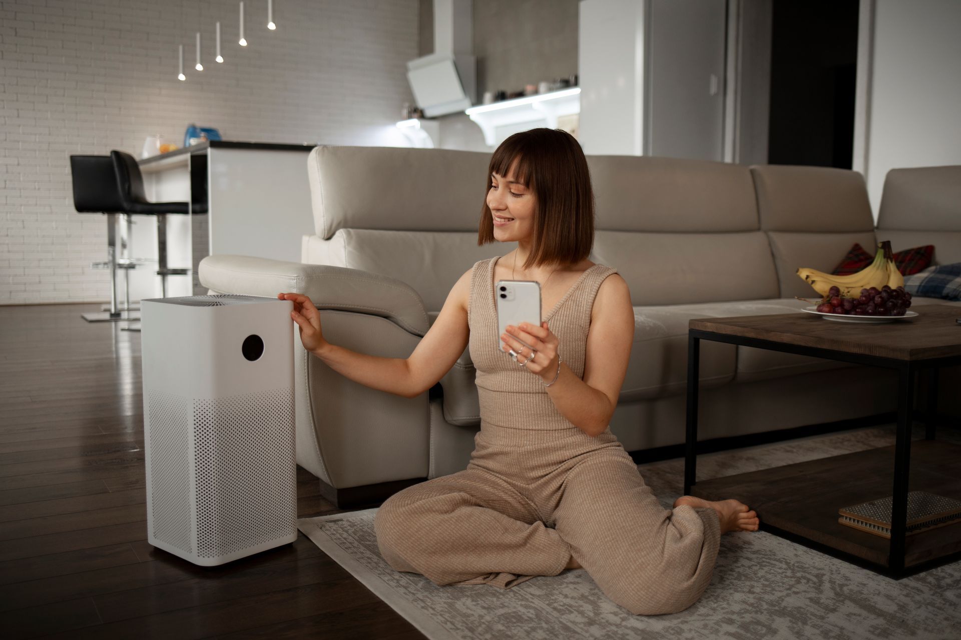 Woman sitting on a rug in a modern living room, smiling at and adjusting a white air purifier