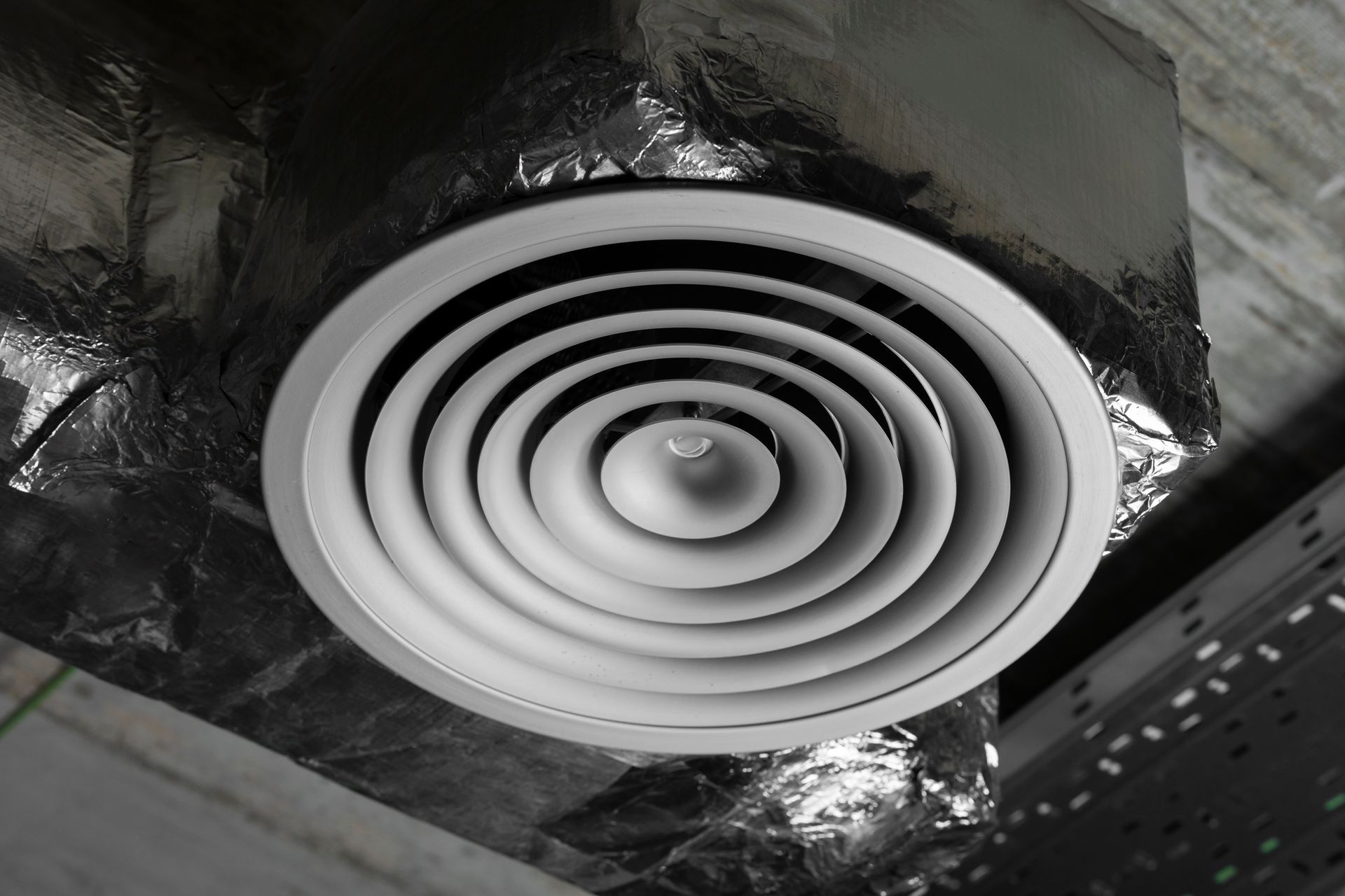 Ceiling-mounted circular air vent, silver and white, surrounded by duct insulation.