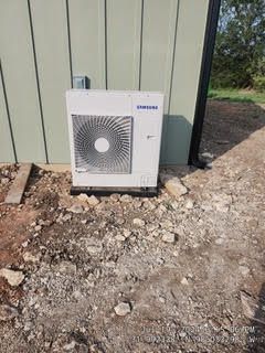 A white air conditioner is sitting on the ground next to a building.