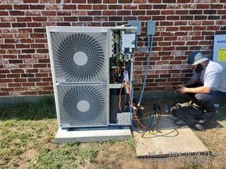 A man is working on an air conditioner outside of a brick building.