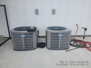 Two air conditioners are sitting next to each other in a garage.