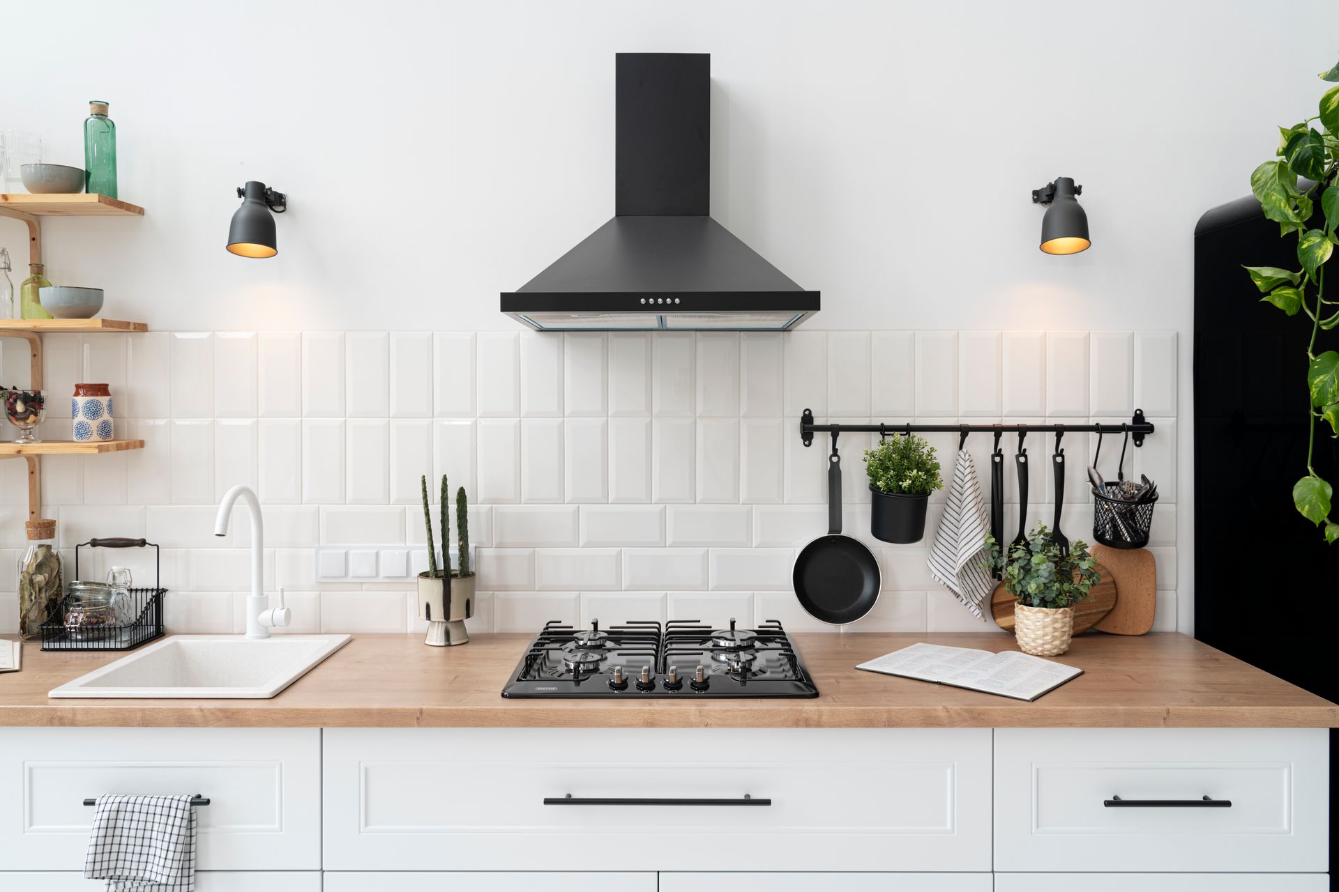A kitchen with white cabinets , a stove top oven , a sink , and a black refrigerator.